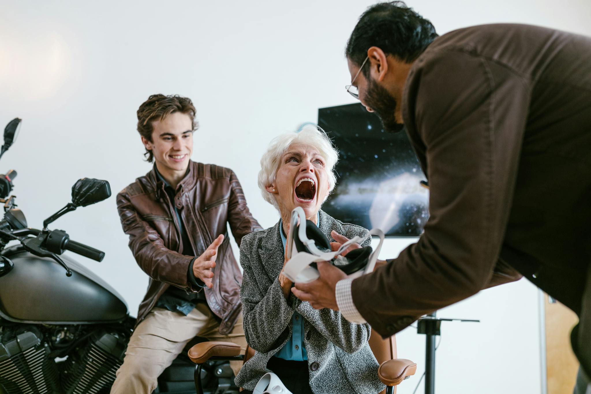 An excited senior woman experiencing virtual reality with the help of two young men indoors.